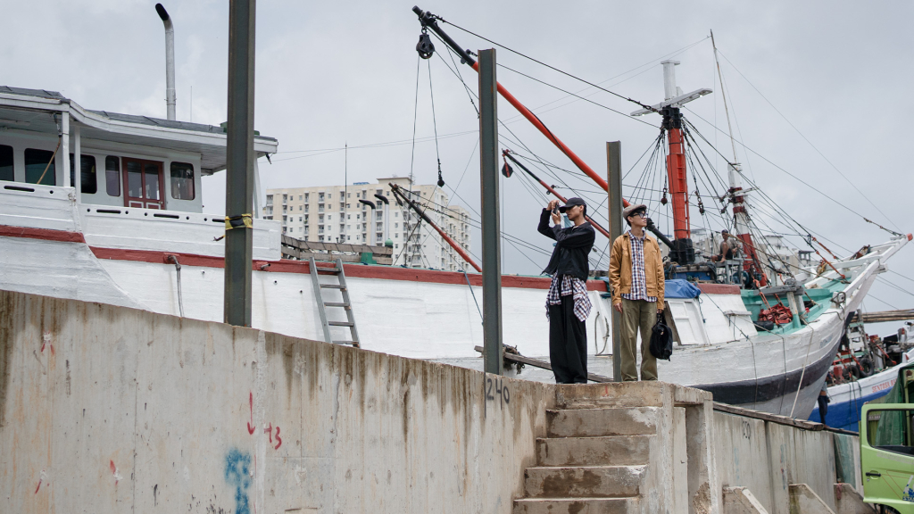 Dua-pria-sedang-walking-tour-depan-kapal-kayu tradisional-Pinisi-bersandar-Pelabuhan-sunda-kelapa-Jakarta-Utara